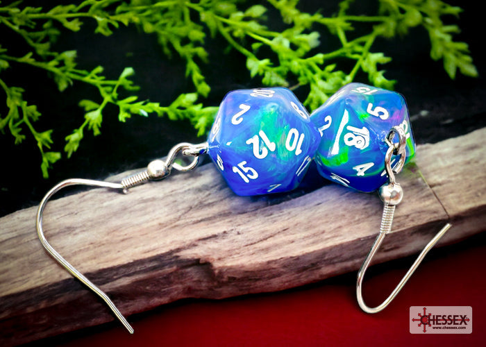 Blue and green polyhedral dice earrings on a wooden surface with green leaves in the background