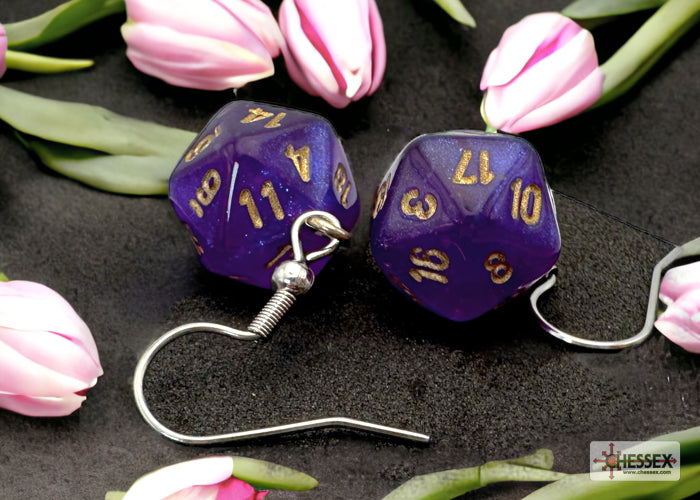 Purple dice-shaped earrings with gold numbers on a dark surface with pink tulips.