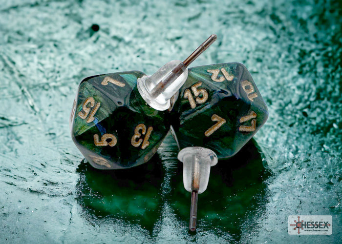 Two green polyhedral dice with gold numbers on a textured green surface, featuring the Chessex brand.