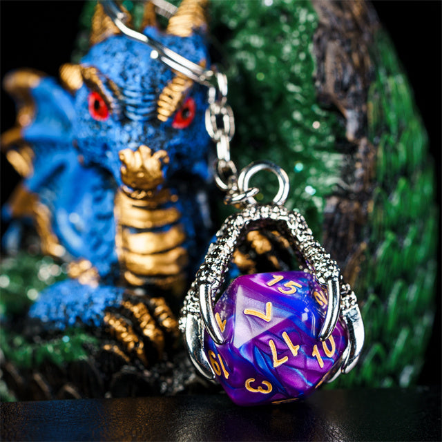 Purple polyhedral dice keychain with chain in front of a blue dragon figurine.