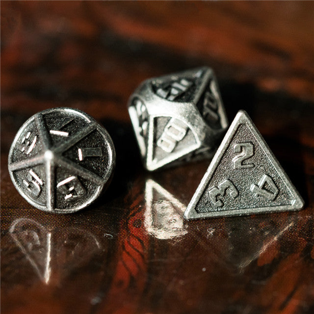 Three metallic polyhedral dice on a reflective surface with a blurred background