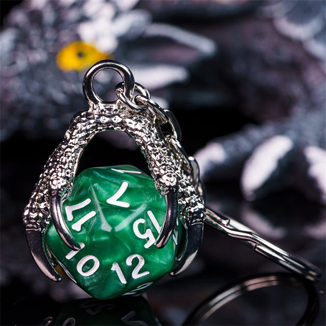 Green polyhedral die charm with silver dragon-like wings on a blurred background