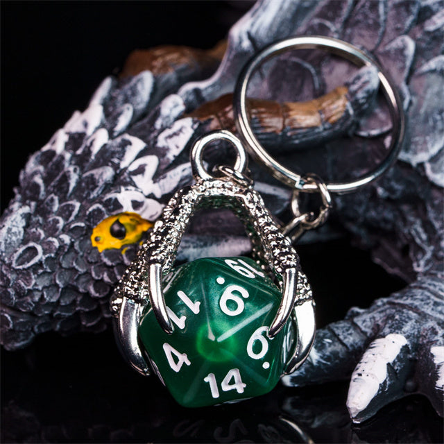 Green polyhedral die keychain with silver dragon claw holder on a textured surface