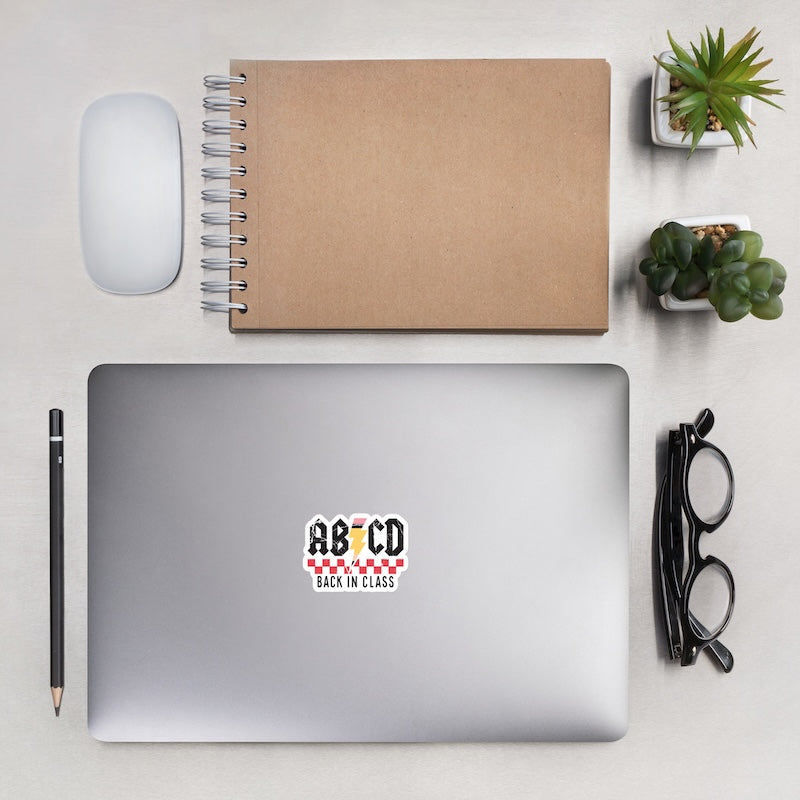 Laptop with a sticker, notebook, mouse, pen, glasses, and plants on a light surface
