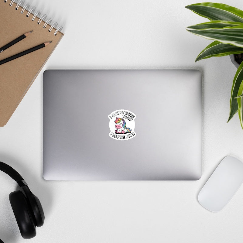 Laptop with a sticker on a desk with a notebook, pens, headphones, and a plant.
