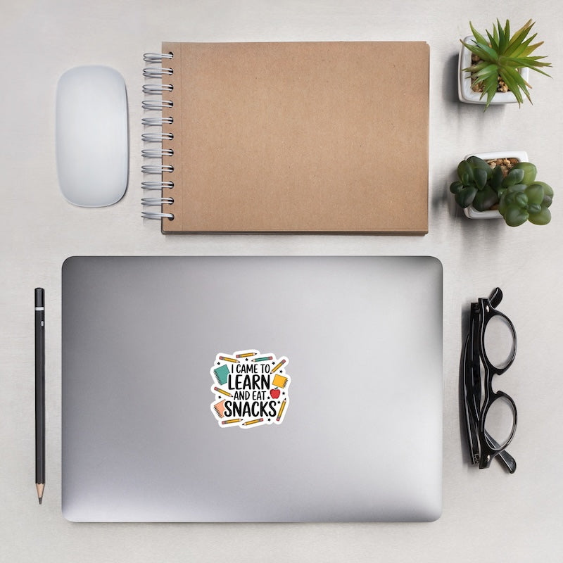 Laptop with a sticker on a desk with a notebook, mouse, pencil, glasses, and plants.