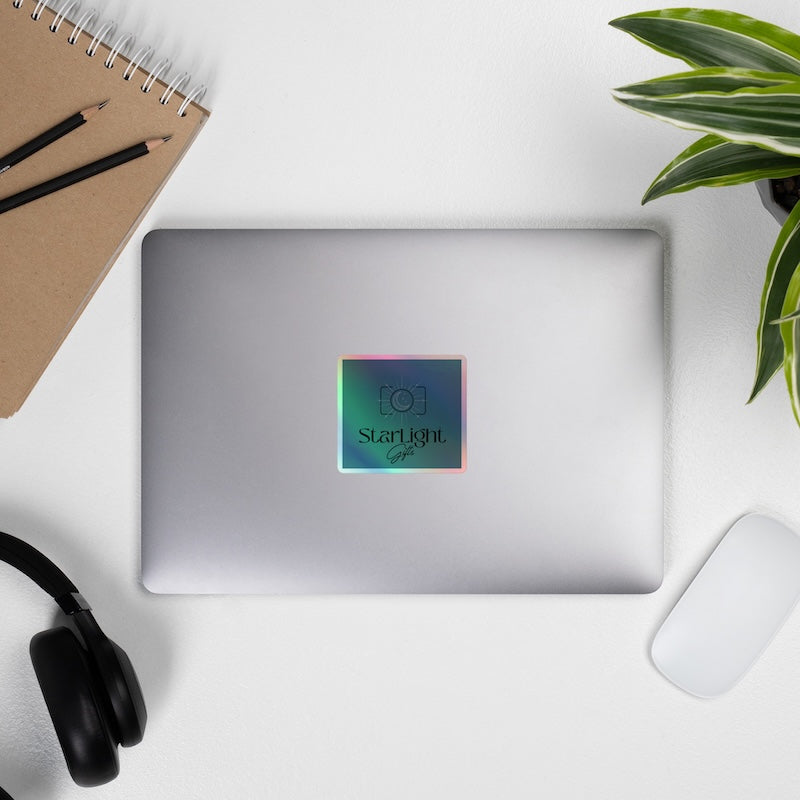 Silver laptop with a colorful 'Starlight' sticker on a white surface with a plant, notebook, and headphones.