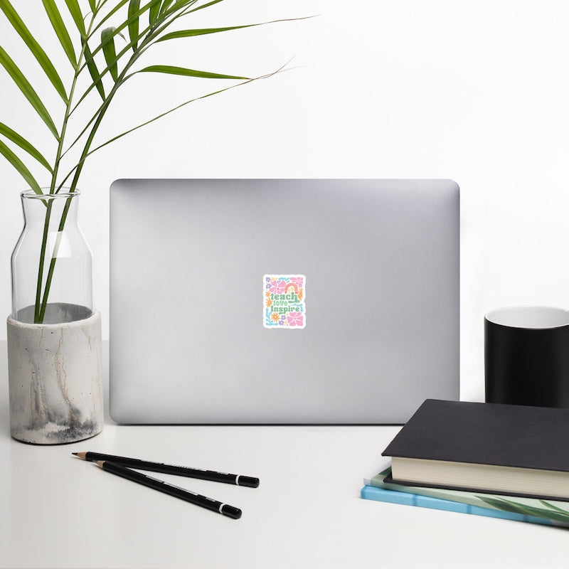 Laptop with a colorful sticker on a desk with a plant, pencils, and books.