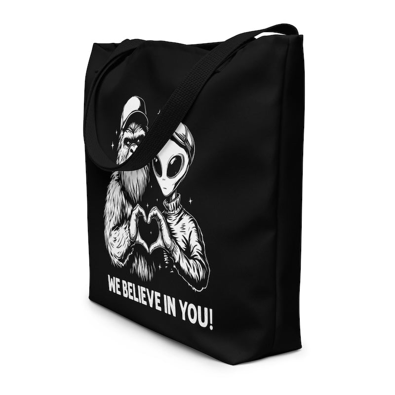 Black tote bag with alien and gorilla design and 'We Believe In You!' text on a white background