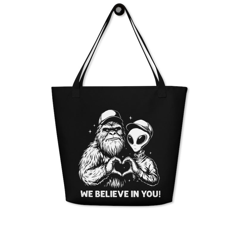 Black tote bag with alien and gorilla design and 'We Believe In You!' text on a white background