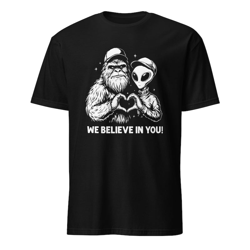 Black t-shirt with a graphic of a gorilla and alien making a heart shape with their hands and text 'WE BELIEVE IN YOU!' on a white background.