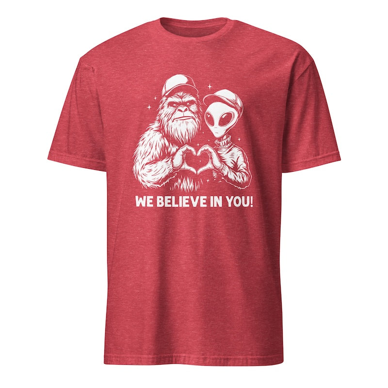 Red t-shirt with a graphic of a humanoid and alien holding hands and 'We Believe In You!' text on a white background.