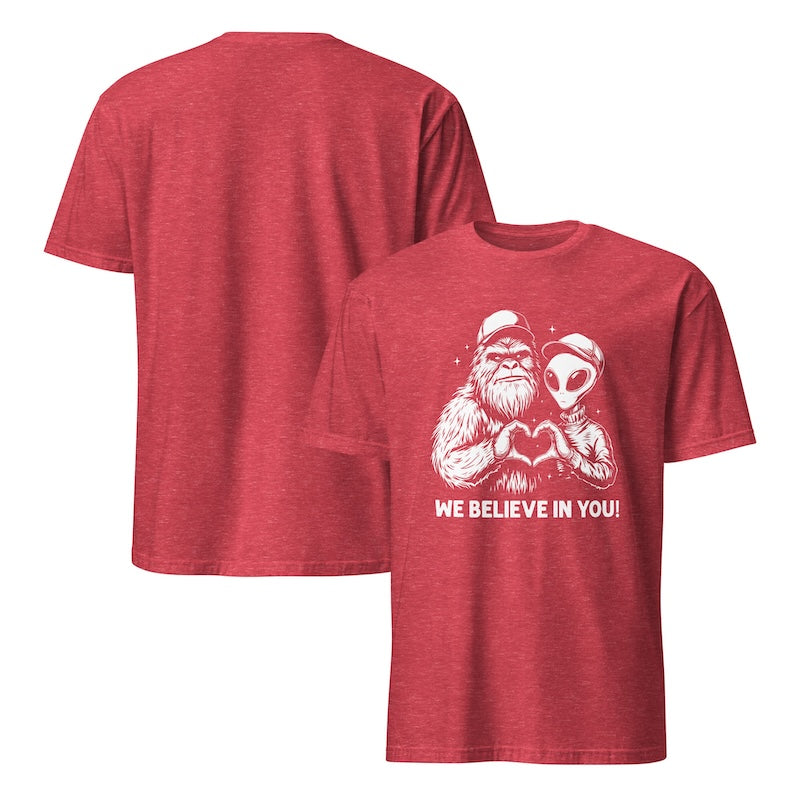Red t-shirt with a graphic design of a bear holding an alien and text 'WE BELIEVE IN YOU!' on a white background.
