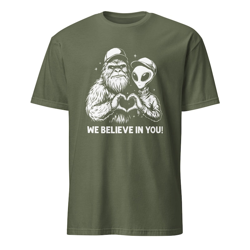 Green t-shirt with a graphic of a Sasquatch and alien making a heart shape with their hands and text 'WE BELIEVE IN YOU!' on a white background.
