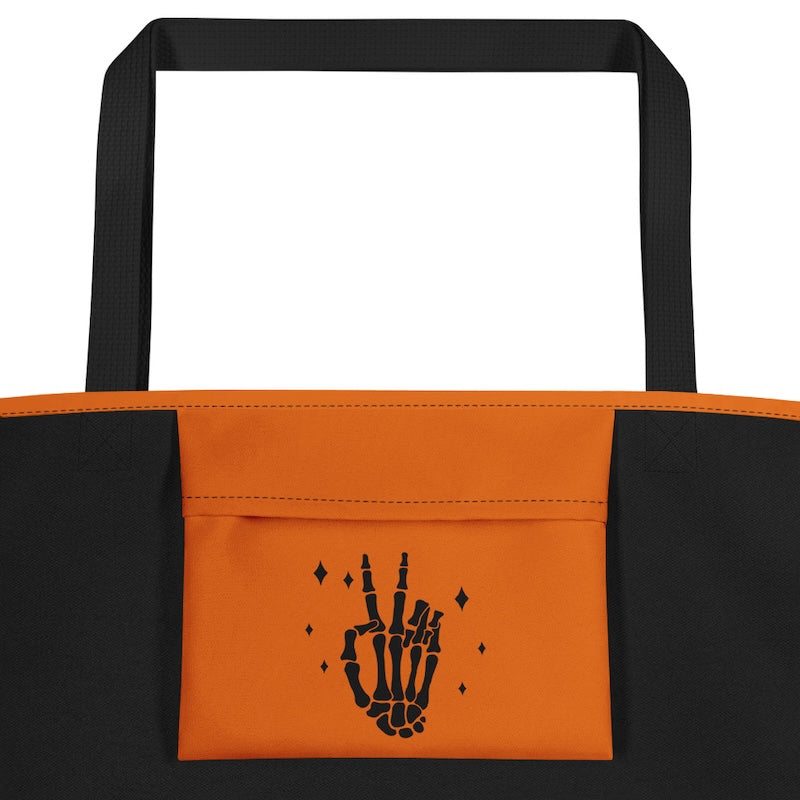 Black and orange tote bag with a skeleton hand design on an orange pocket.