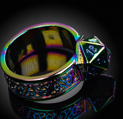 Multicolored ring with intricate design and a polyhedral die on a reflective surface.