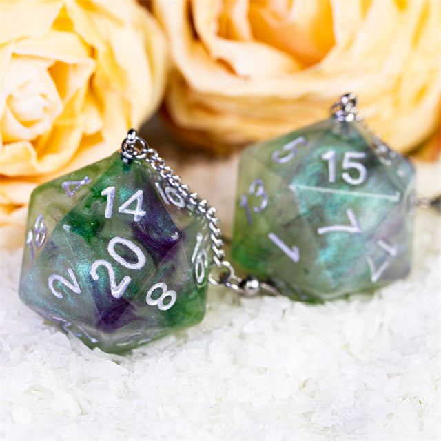 Two green polyhedral dice with chain on a white surface with yellow roses in the background