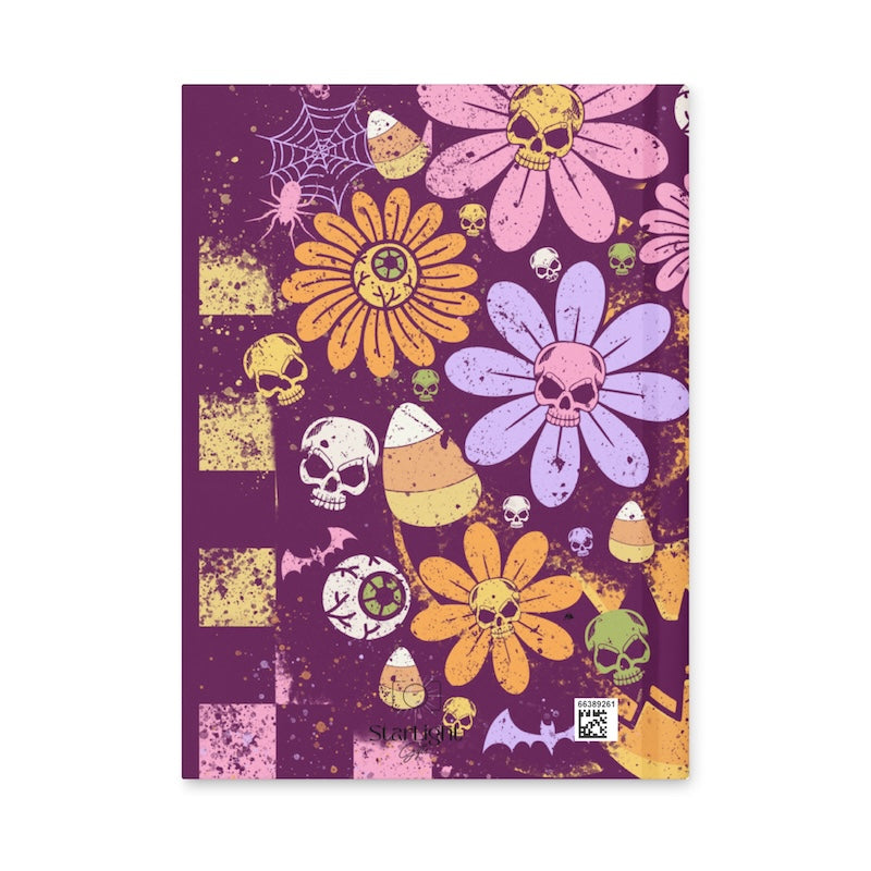 Notebook with Halloween-themed design featuring flowers, skulls, and candy corn on a purple background.