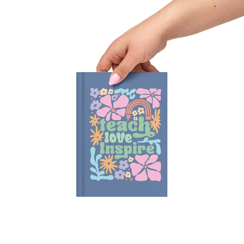 Hand holding a notebook with floral design and 'teach love inspire' text on a white background
