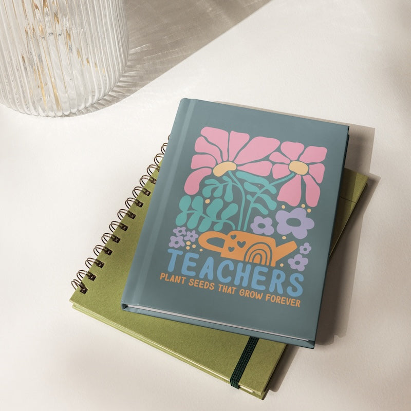 Notebook with floral design and 'Teachers Plant Seeds That Grow Forever' text on a white surface