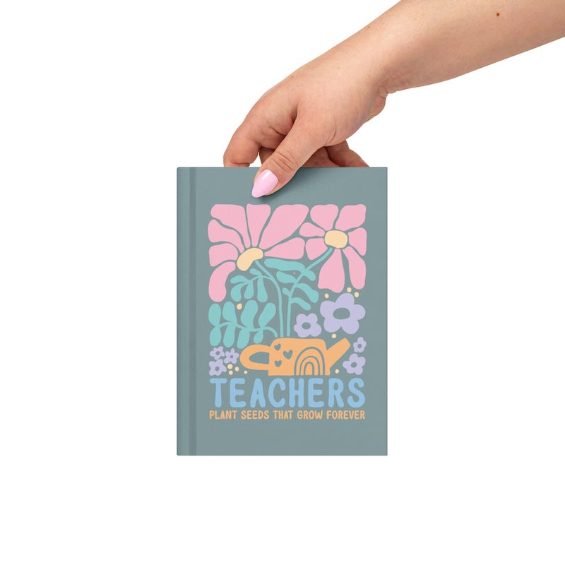 Hand holding a notebook with floral design and 'Teachers' text on a white background