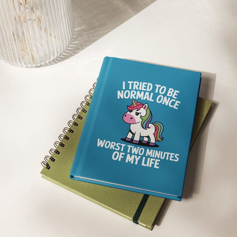 Blue notebook with unicorn illustration and humorous text on a white surface