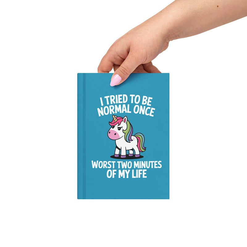 Blue notebook with a unicorn illustration and text held by a hand on a white background