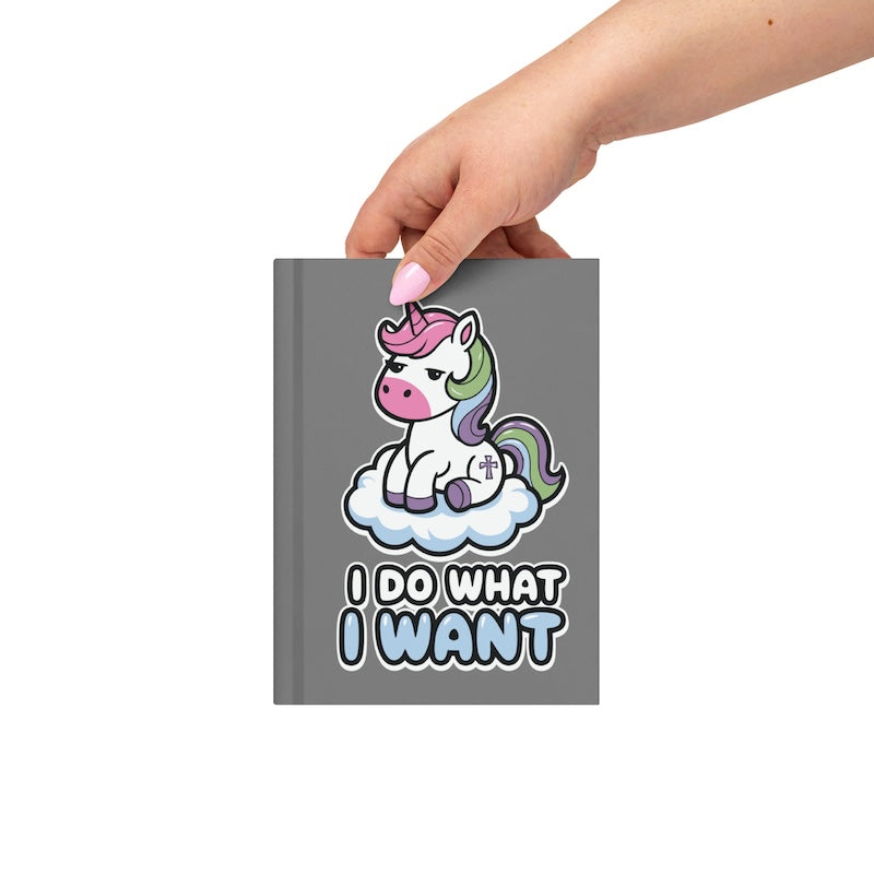 Gray notebook with a unicorn design and text, held by a hand on a white background