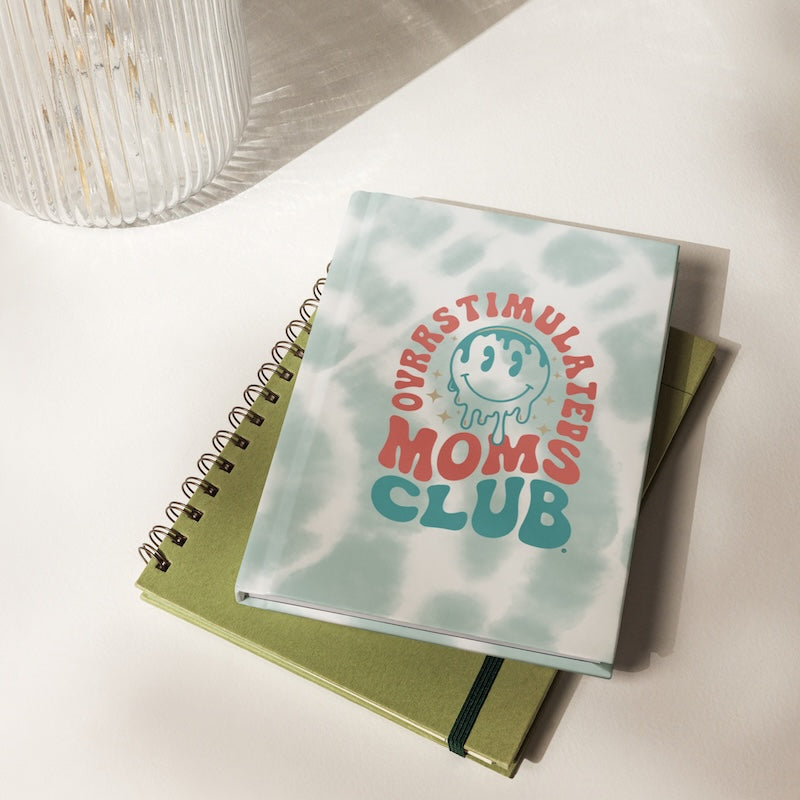 Notebook with 'Overstimulated Moms Club' cover on a light surface
