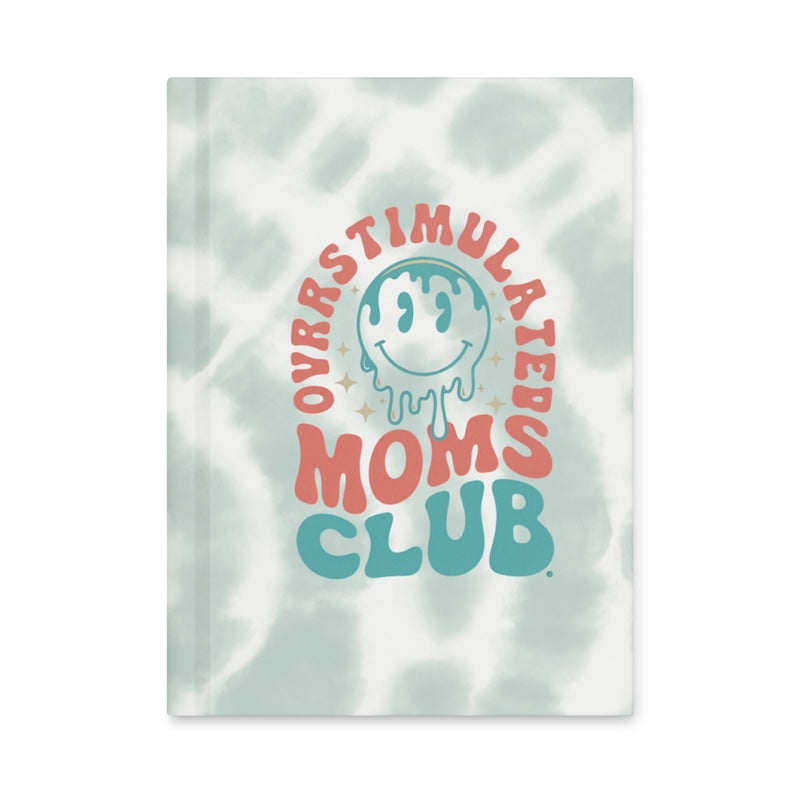 Book or notebook with 'Overstimulated Moms Club' text and smiley face on a light patterned background