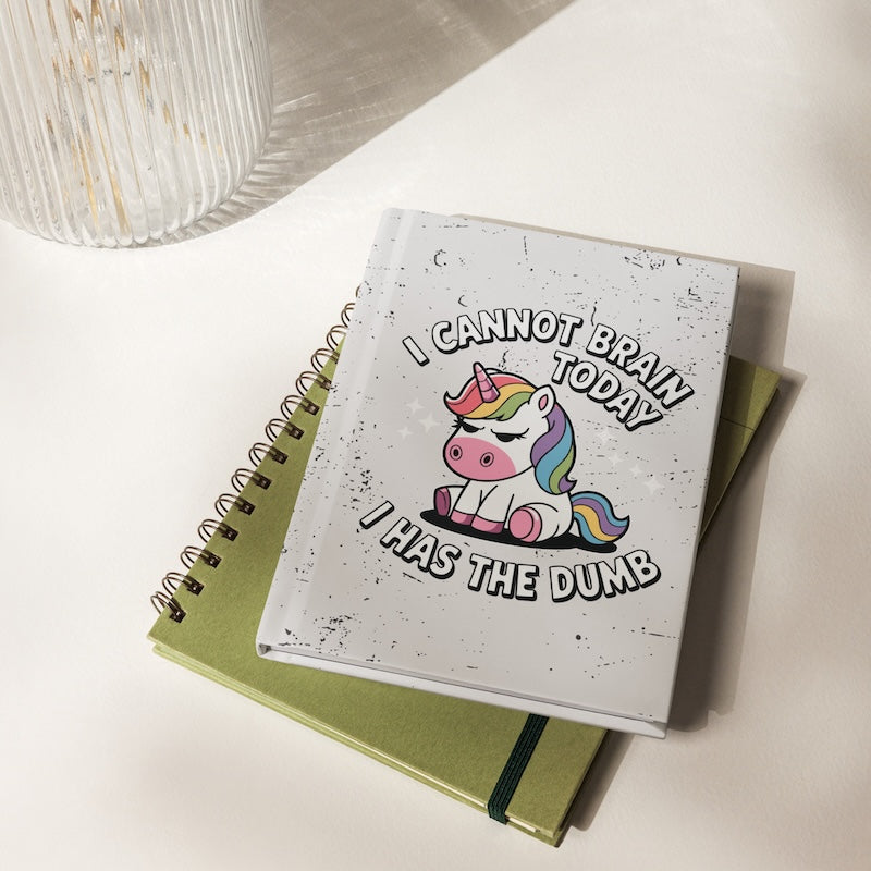 Notebook with a unicorn illustration and humorous text on a light surface
