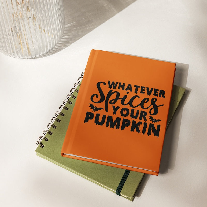 Orange notebook with 'Whatever Spices Your Pumpkin' text on a white surface