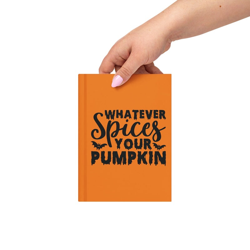 Orange notebook with 'Whatever Spices Your Pumpkin' text held by a hand on a white background