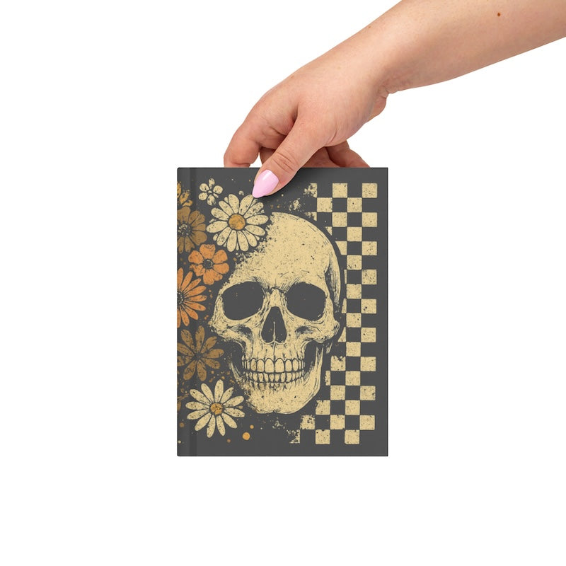 Notebook with skull and floral design held by a hand on a white background