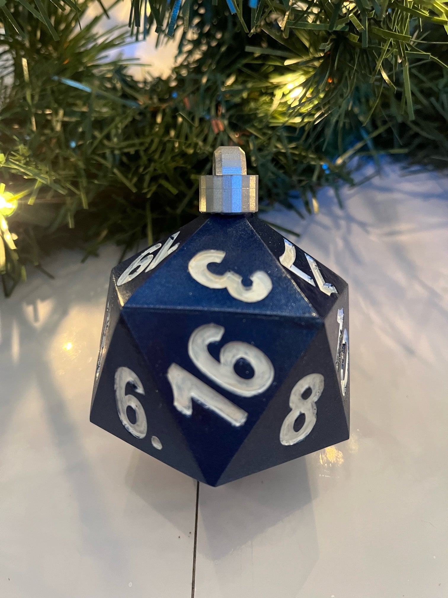 Blue D20 dice ornament with white numbers on a Christmas tree background