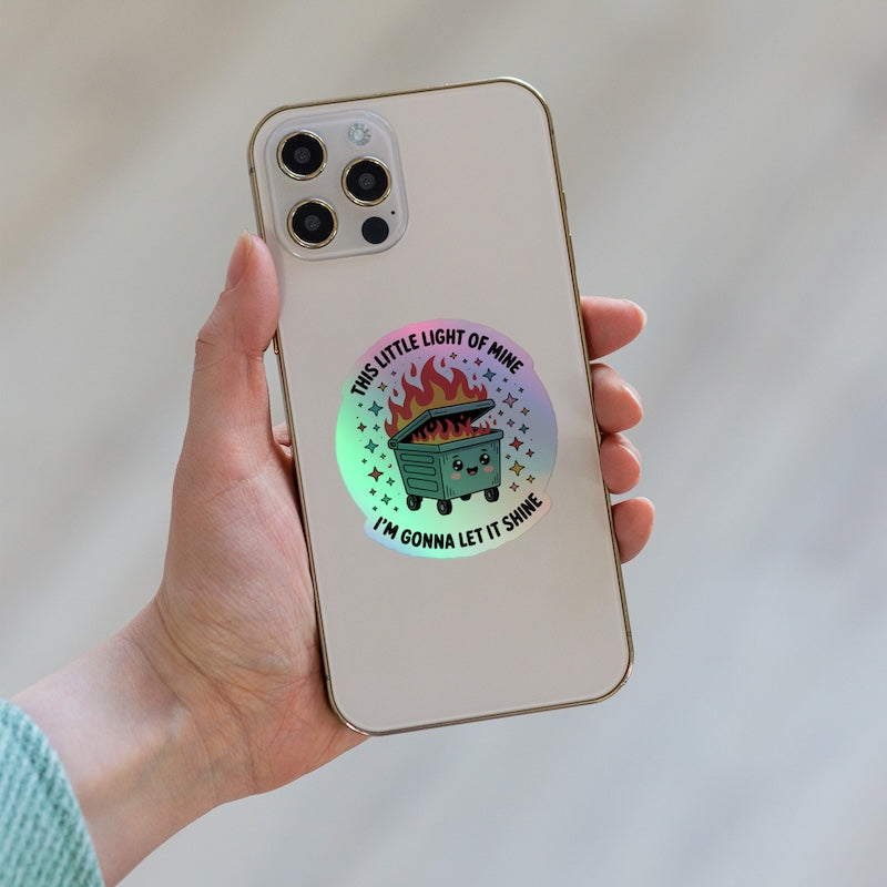 Phone case with a design of a cartoon trash can and text, held by a hand against a neutral background.