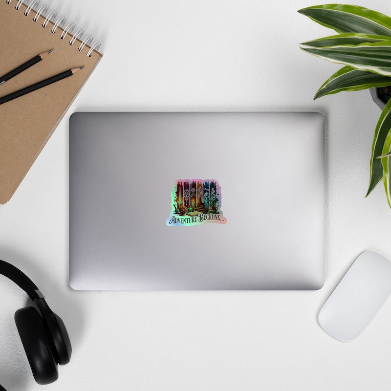 Silver laptop with a colorful sticker on a white surface with a plant, notebook, and headphones.