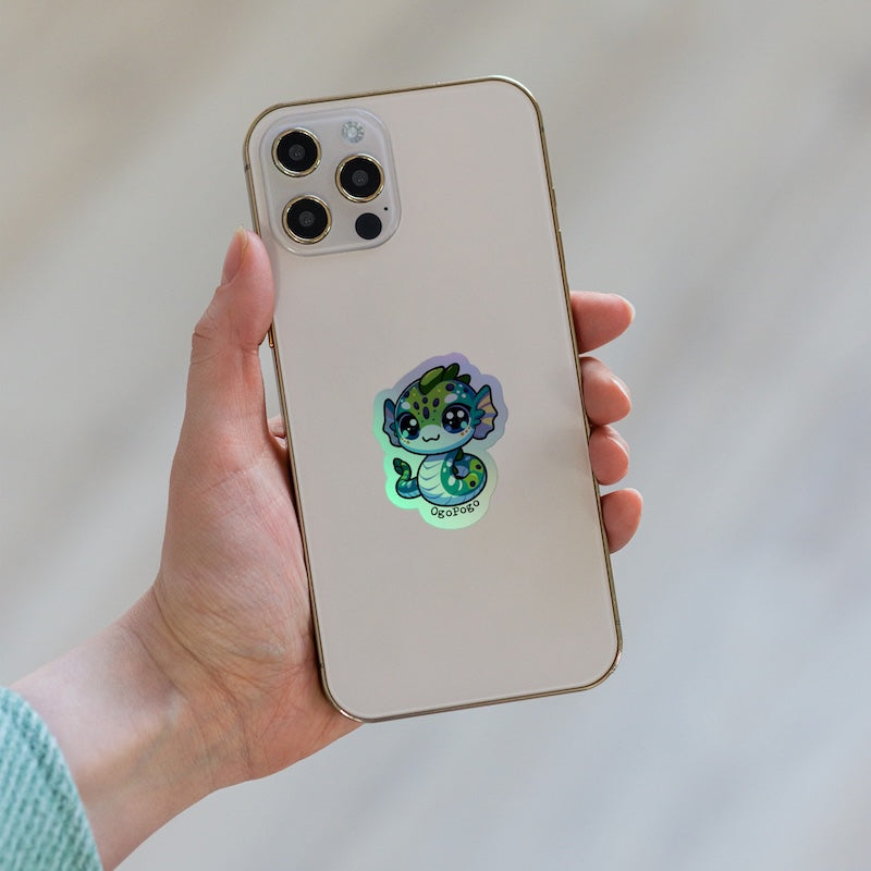 Phone case with a cute green creature design held by a hand against a neutral background