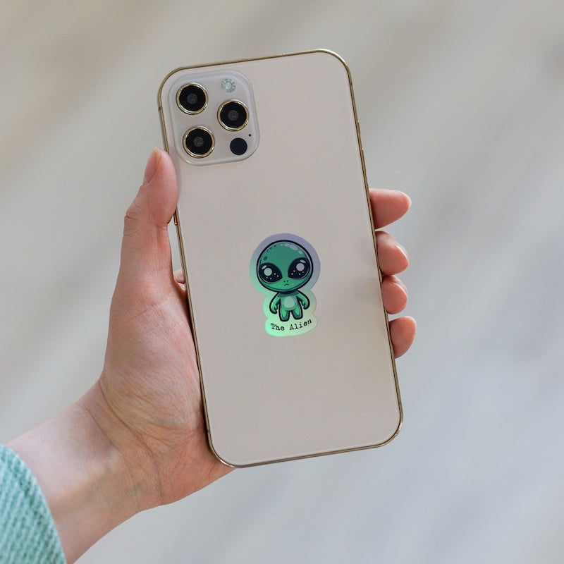 Phone case with a green alien design held by a hand against a neutral background
