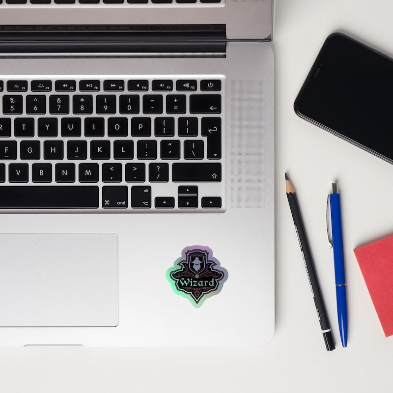 Laptop with a 'Wizard' sticker, phone, pencil, pen, and notebook on a white surface