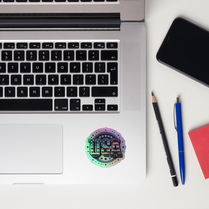Laptop with a 'USA' sticker, phone, and writing utensils on a white surface