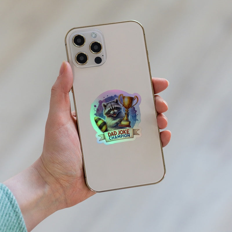 Phone case with a raccoon illustration and 'Dad Joke Champion' text held by a hand.