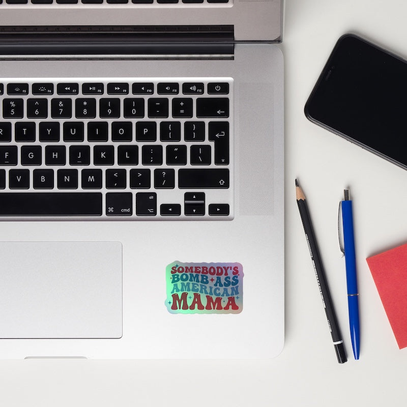Laptop with a colorful sticker on a white surface, surrounded by a phone, pen, and pencil.