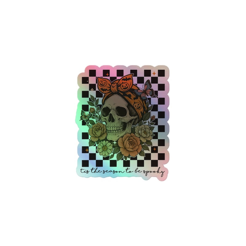 Holographic sticker with a skull, roses, and pumpkins design on a checkered background.