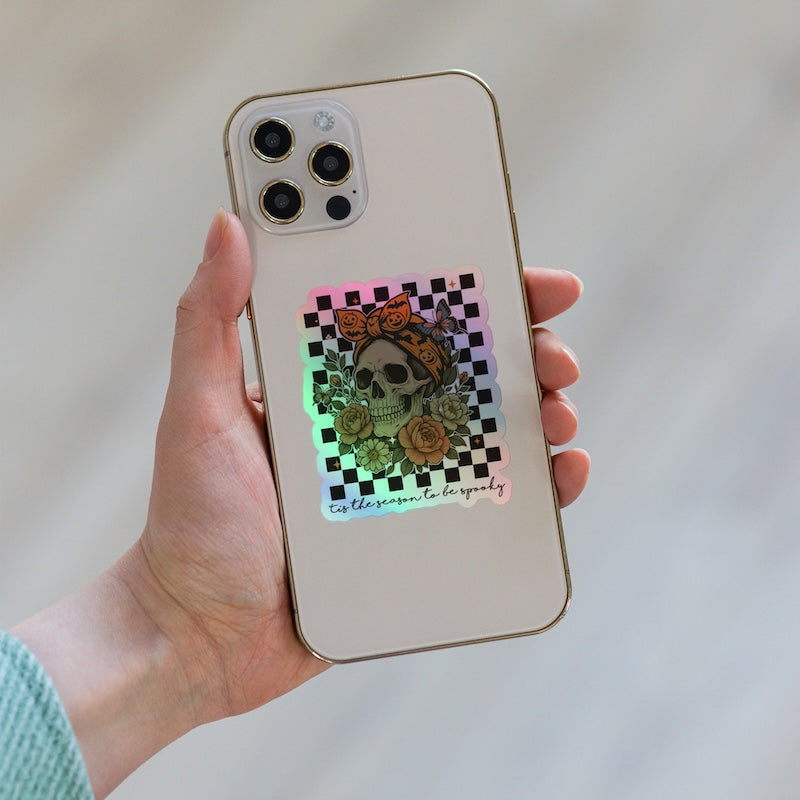 Phone case with a skull and roses design held by a hand against a neutral background