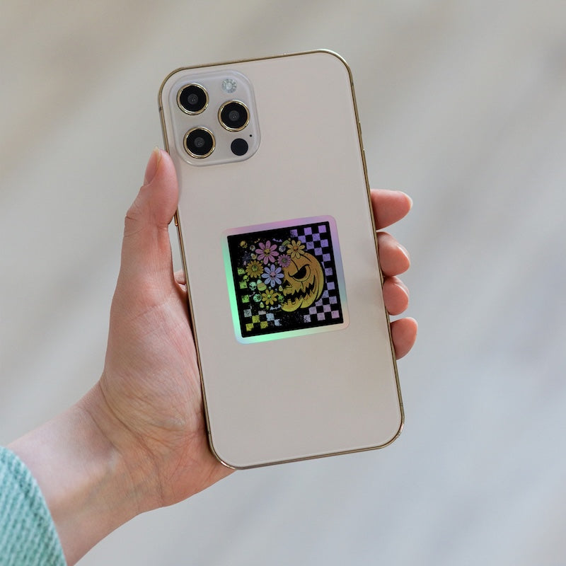 Hand holding a phone with a colorful case featuring a design of a cat and flowers on a light background.