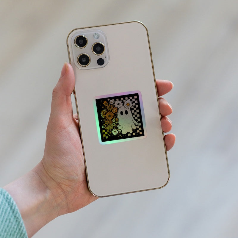 Hand holding a phone with a ghost design on the screen against a neutral background