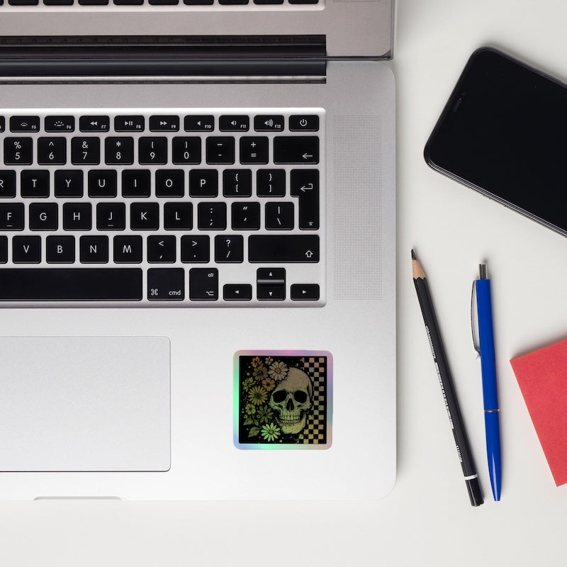 Laptop with a skull design card, pencil, pen, and notebook on a white surface
