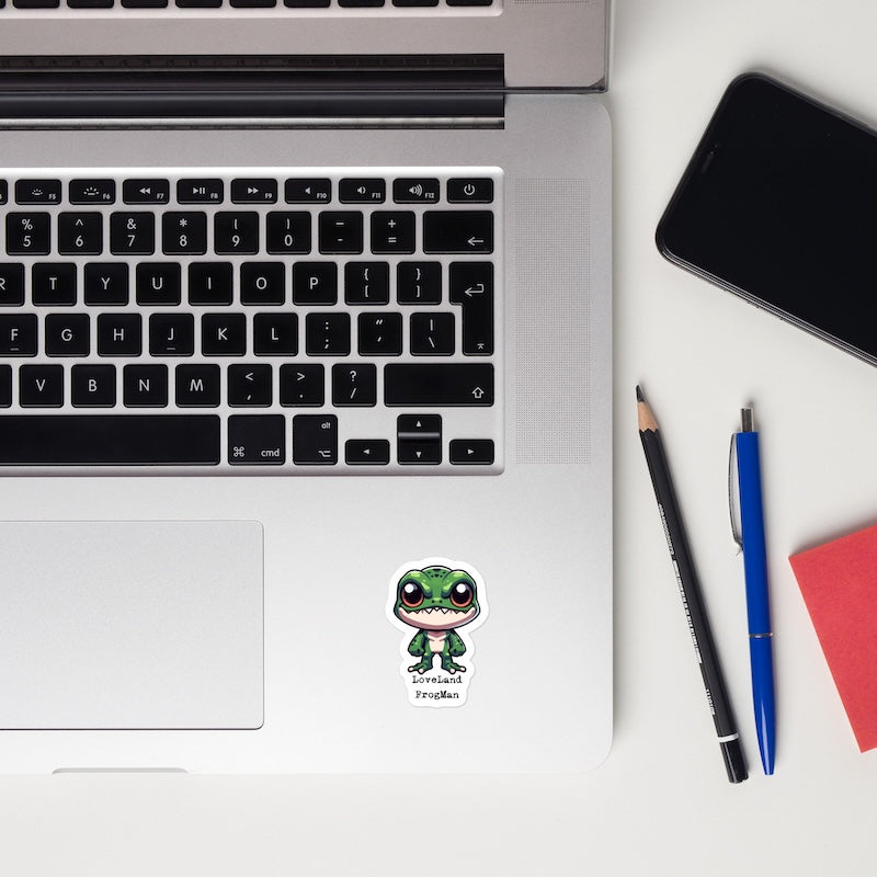 Laptop with a sticker on a white surface, next to a phone, pencil, and pen.