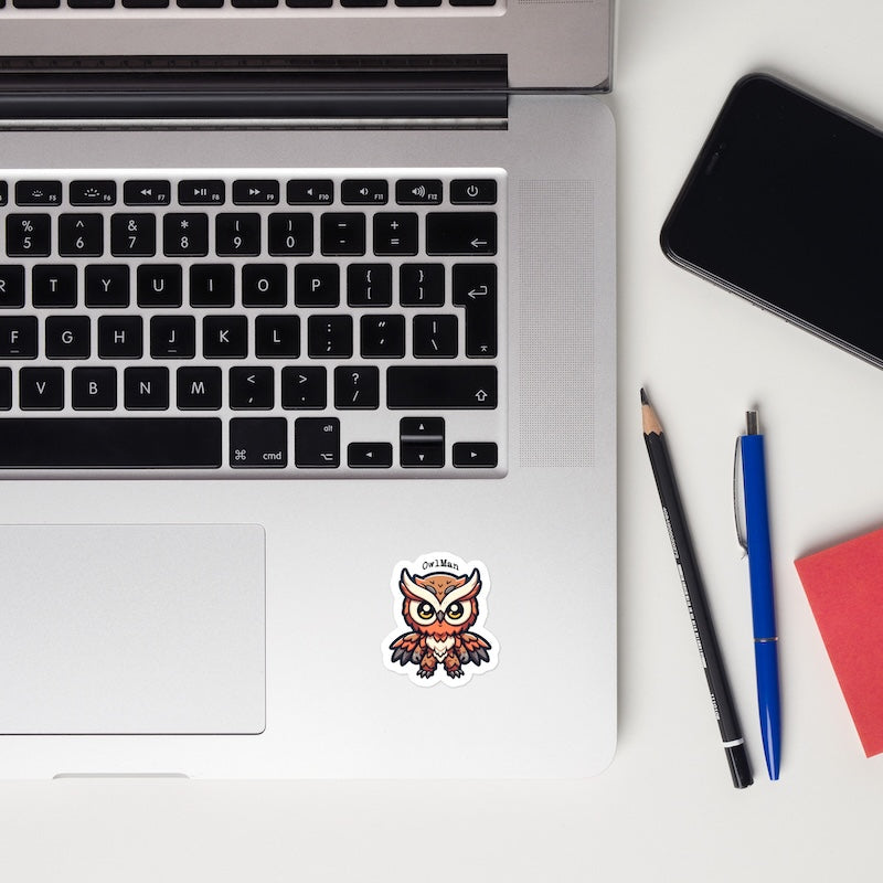 Laptop with owl sticker, phone, pencil, pen, and notebook on a white surface